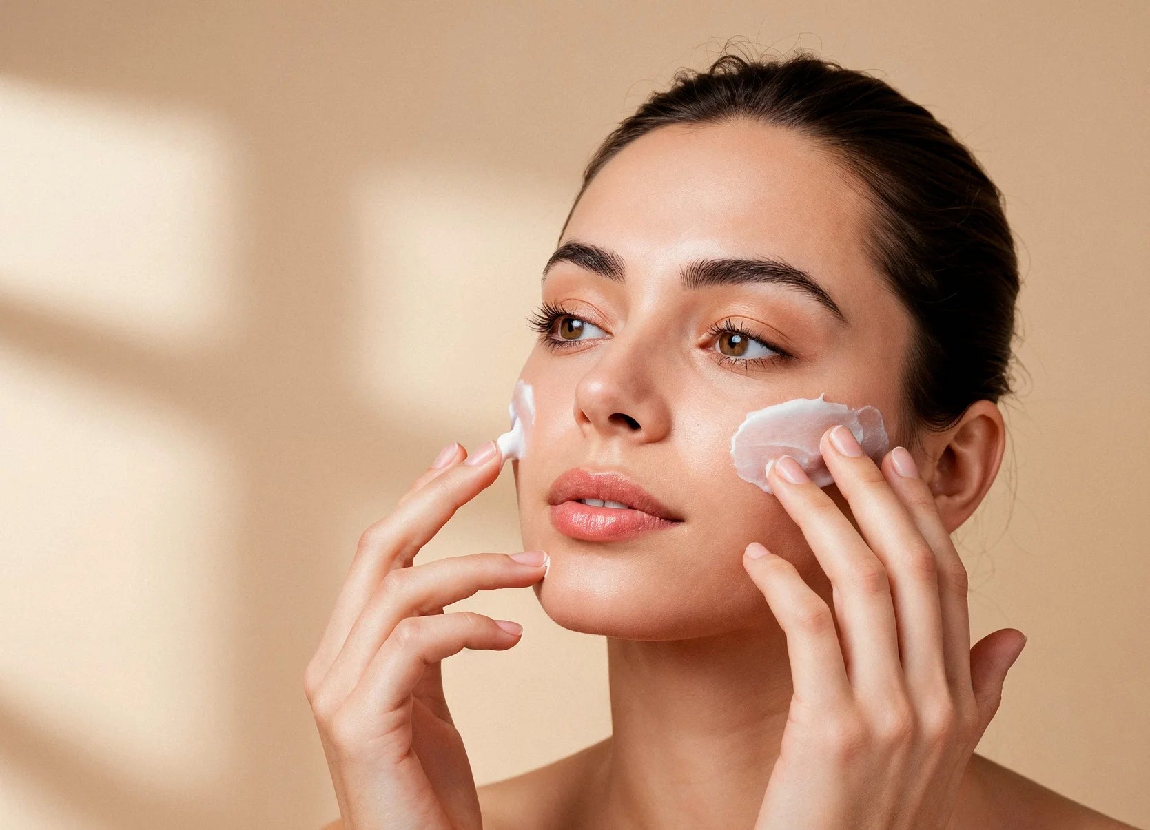 Woman applying cream to her face with a beige background